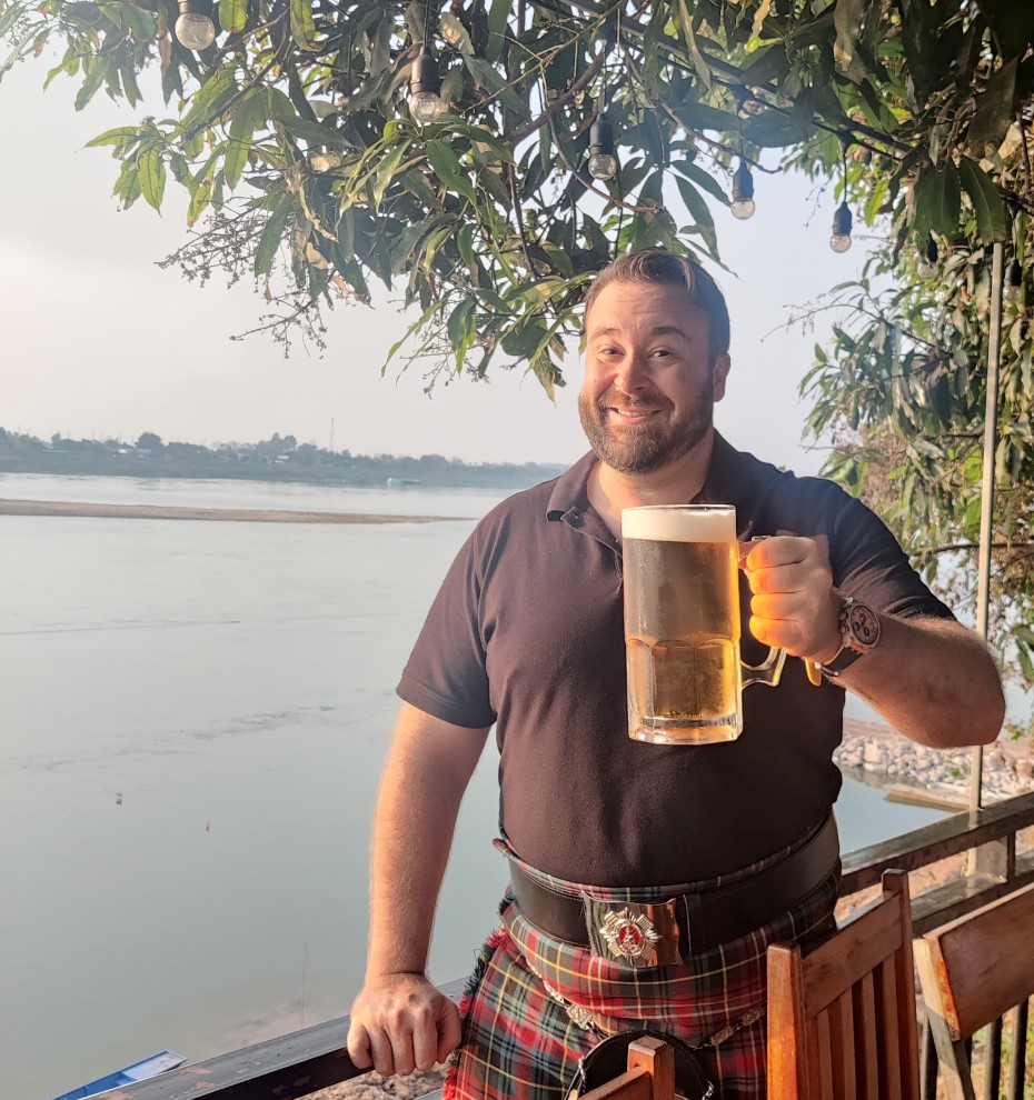 Man in kilt with a big mug of cold beer overlooking the wide Mekong River