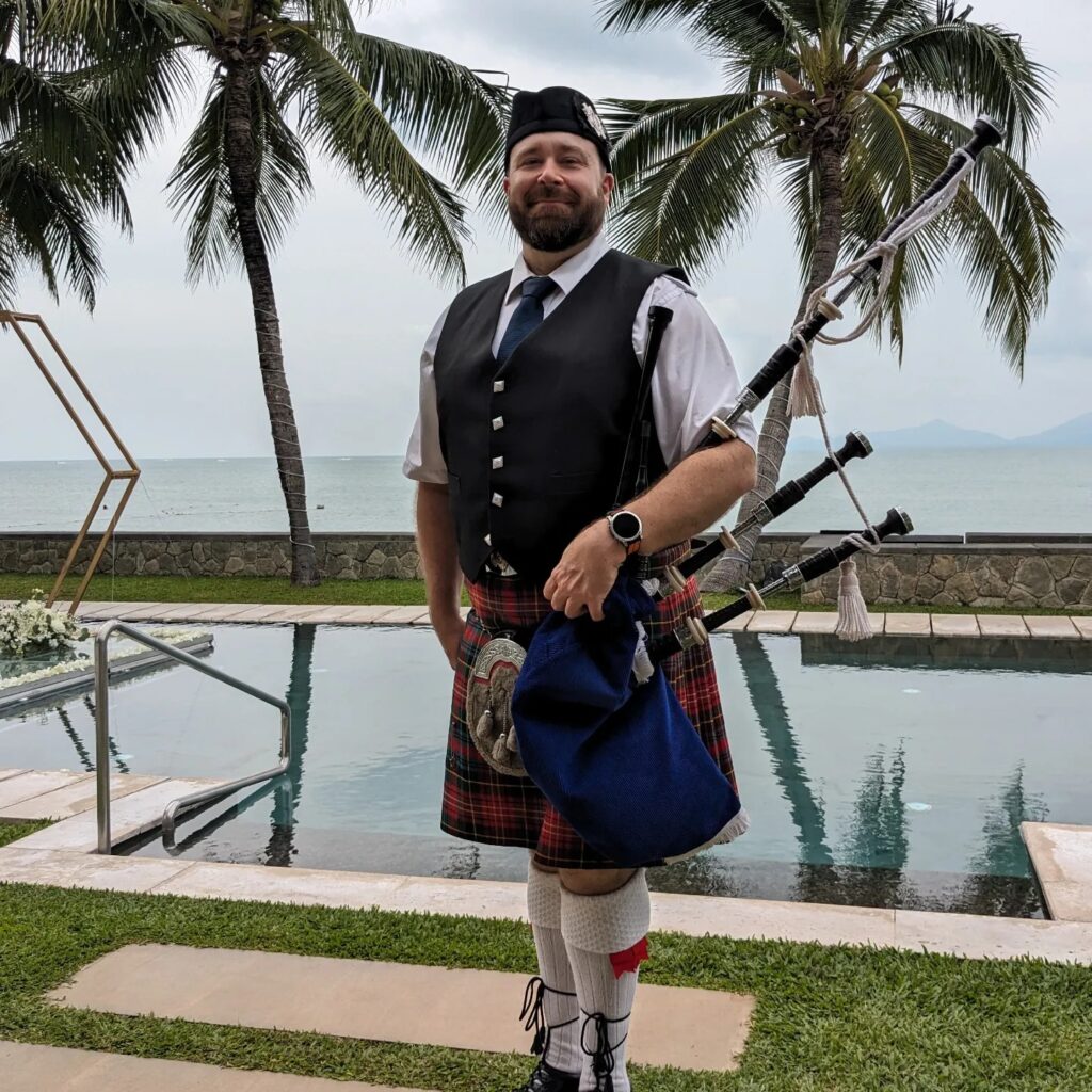 Bagpiper standing in front of a pool next to palm trees by the water in Koh Samui Thailand. 